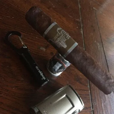 A CAO Flathead Steel Horse cigar on a wooden table beside a cutter and a lighter
